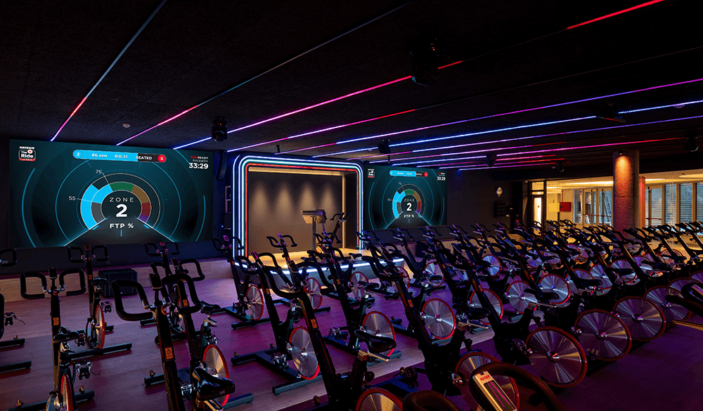 Render of an indoor cycling studio class with Keiser's The Ride studio projected on the screens in background