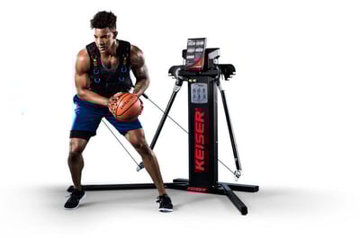Man with a functional training vest tethered to a Keiser Functional Trainer holding a basketball, mimicking an on-court move.