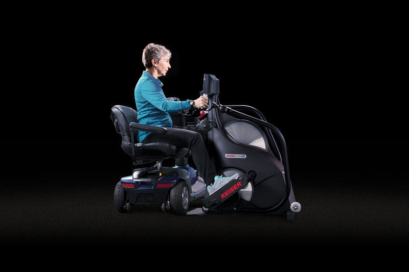 Woman in a assistive scooter pulled up to a Keiser M7i Total Body Wheelchair Accessible Stepper